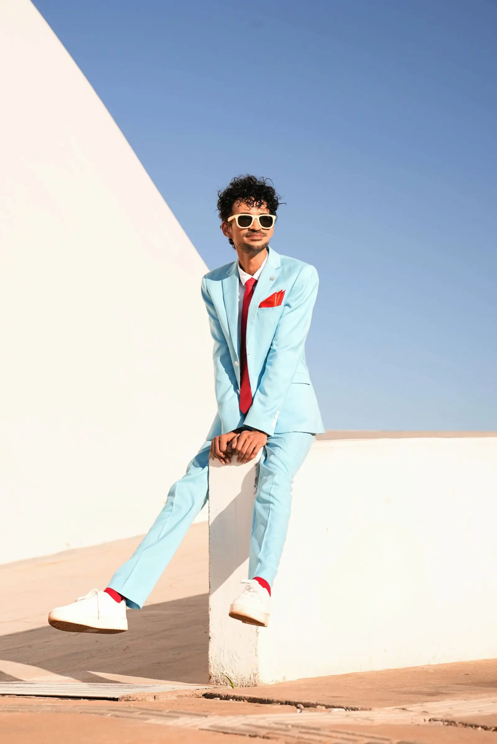 Marlon seated on a white plinth in a pale blue suit