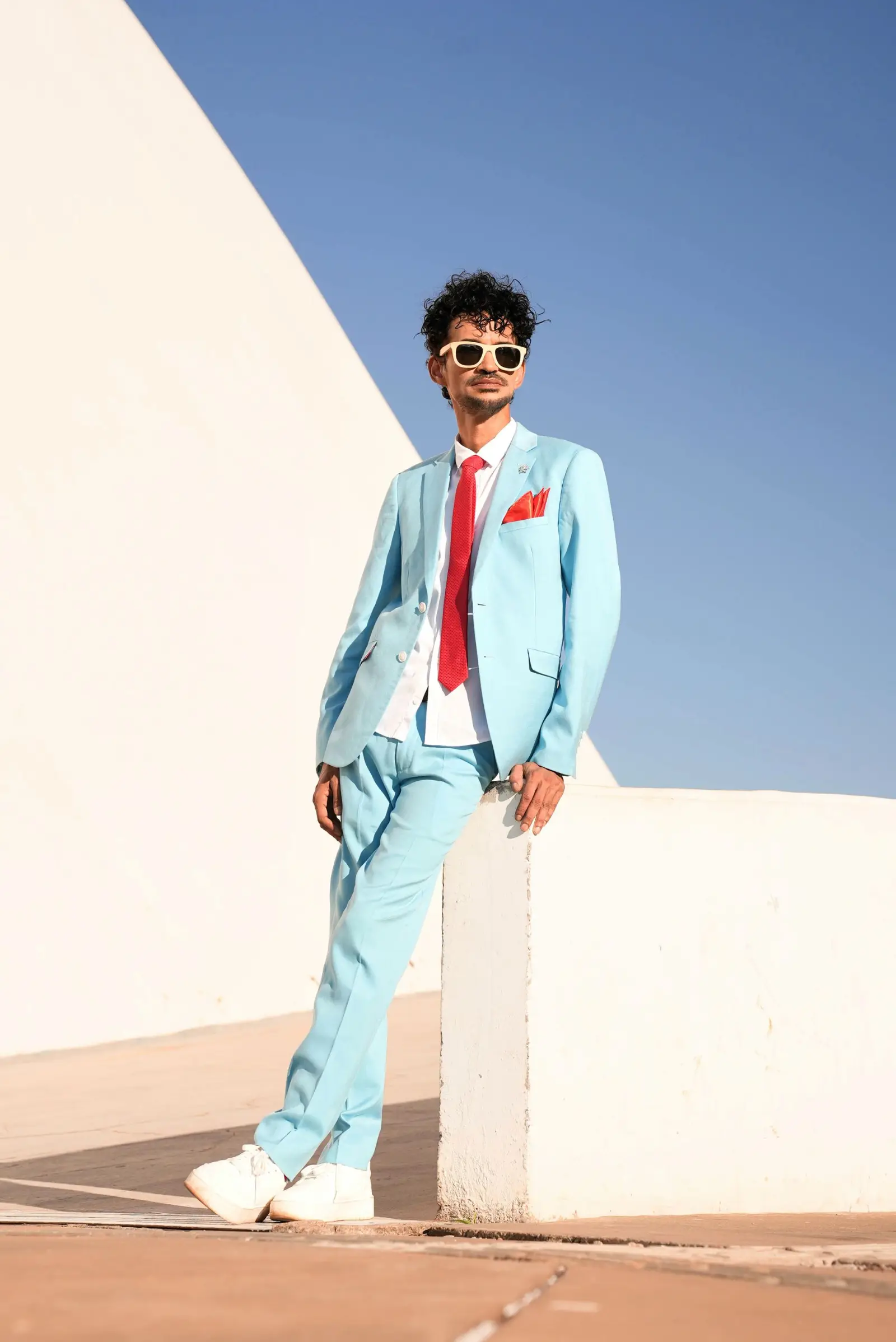 Marlon Claessen in a pale blue suit against a white curved wall and blue sky