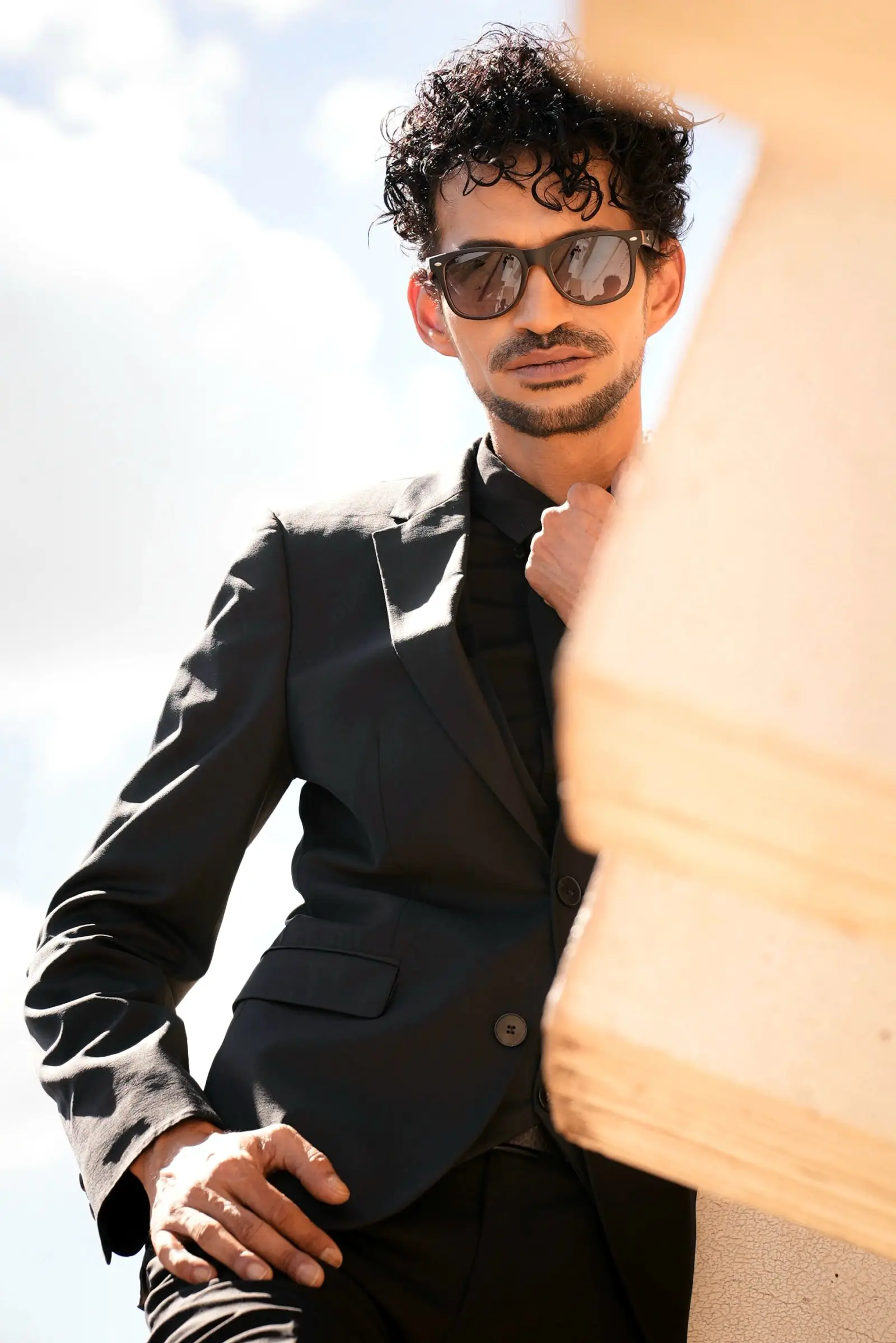 Portrait of Marlon Claessen in a black suit and sunglasses, sunlight on his face
