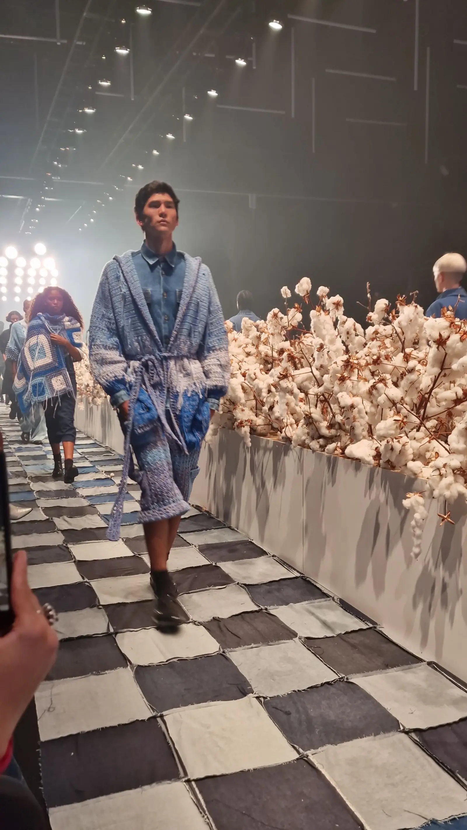 Model on a checkerboard runway lined with dried flowers