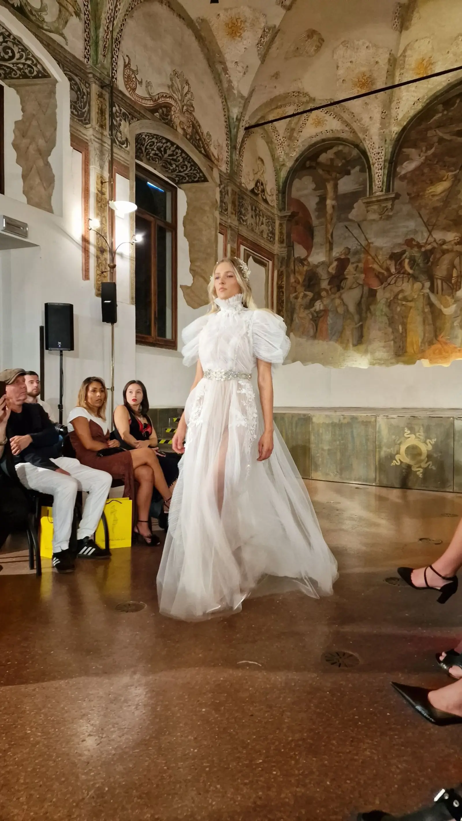 A model in a voluminous white gown walking beneath painted frescoes