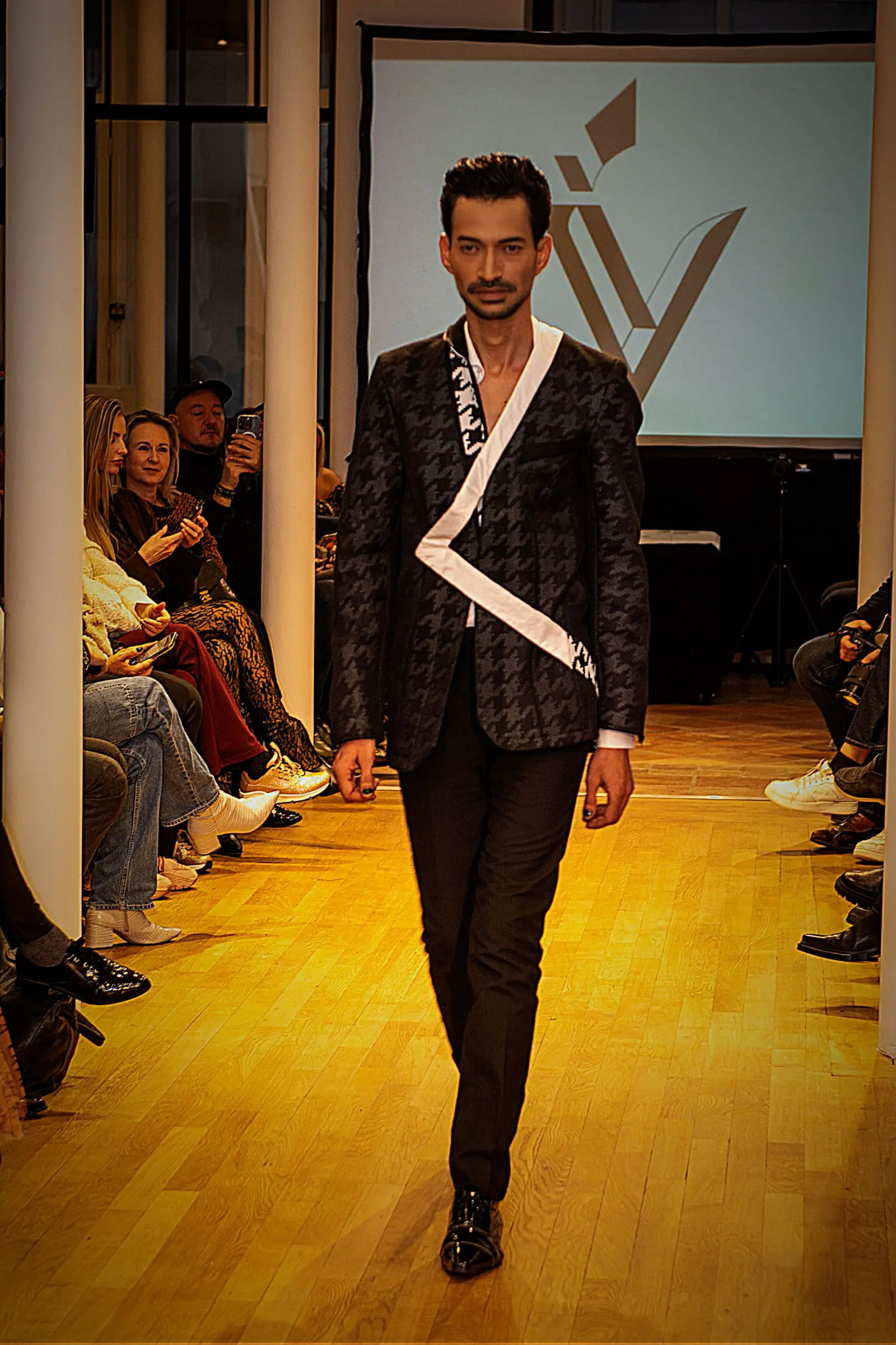 Marlon walking a runway in a black jacket with white piping