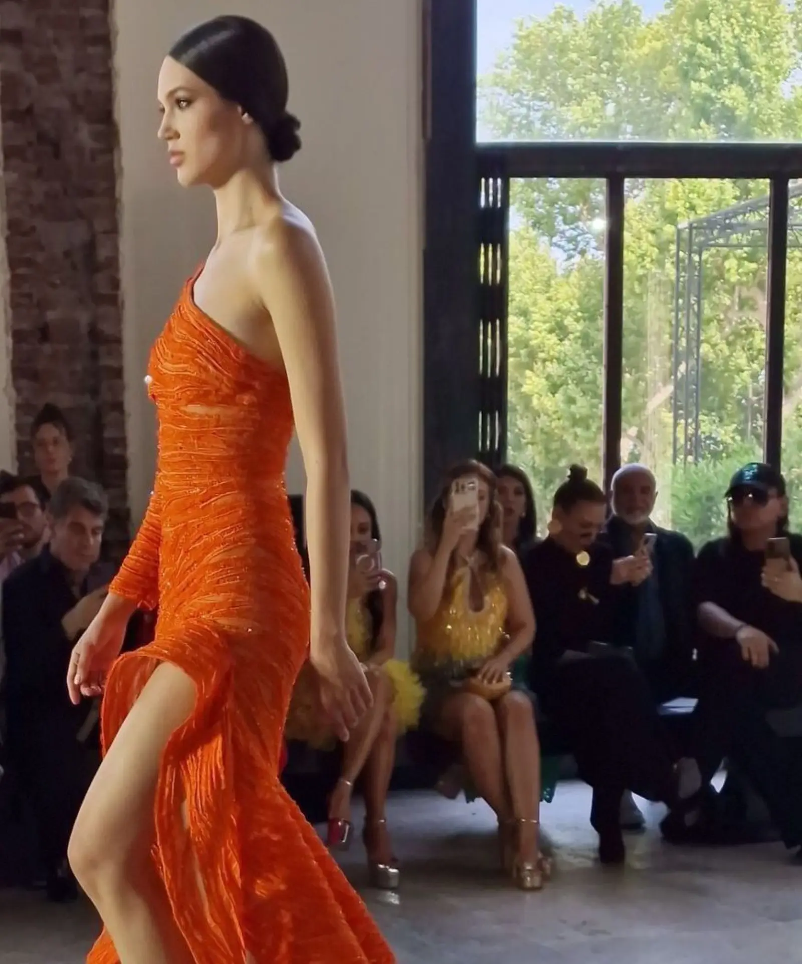 Model in a draped orange gown walking past the front row