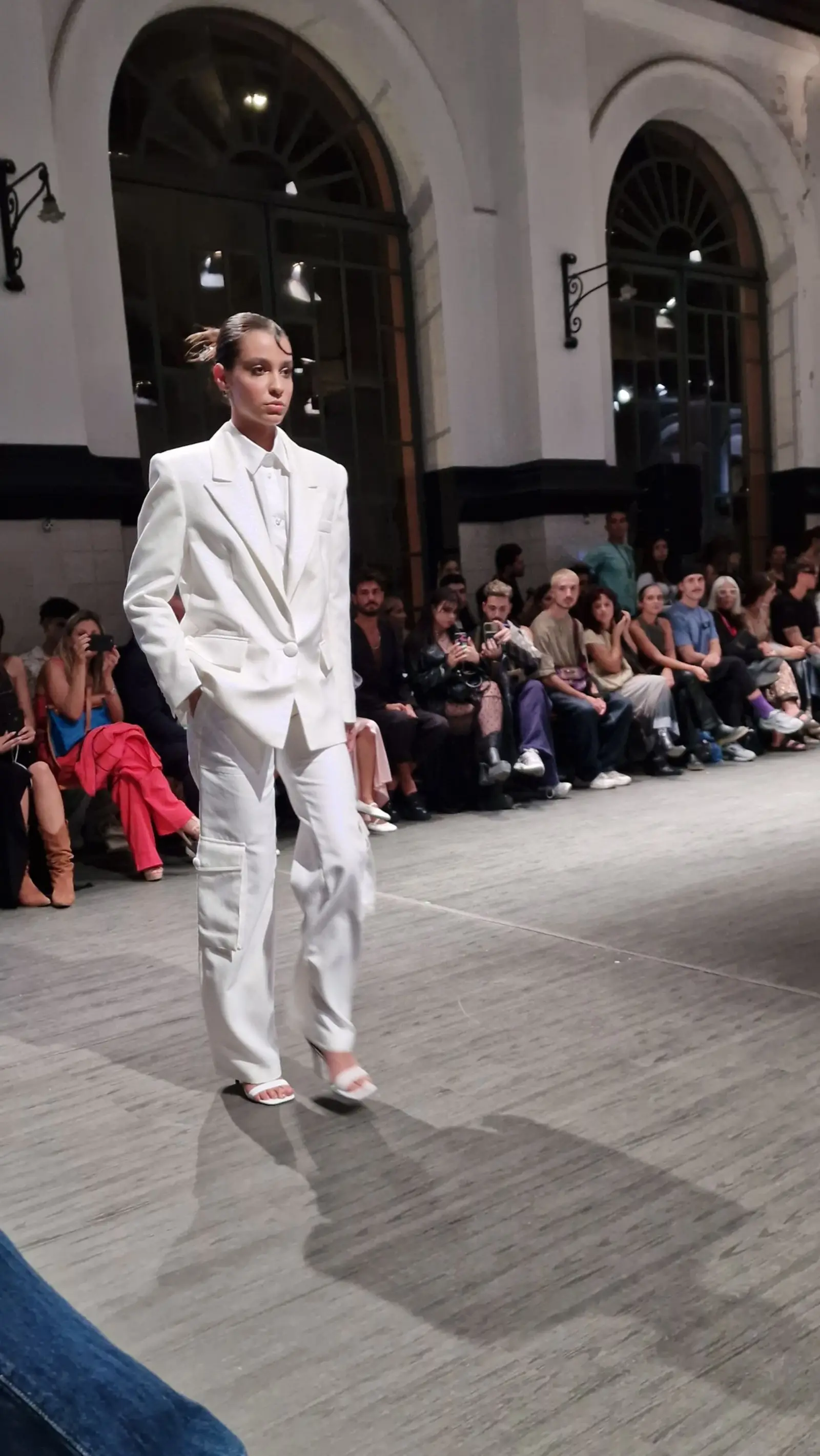 Model in an all-white suit on a runway in a vaulted hall